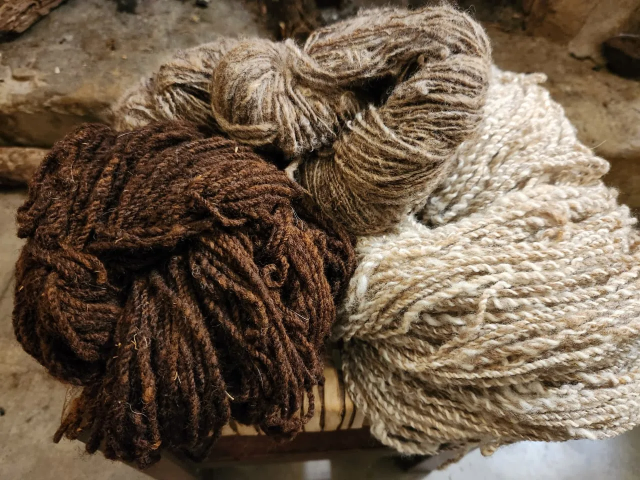 Tres madejas de lana hilada a mano: marrón, gris y crudo